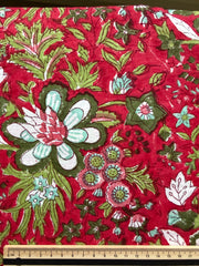 Floral fabric with green and white flowers on a red background, measured by a ruler.