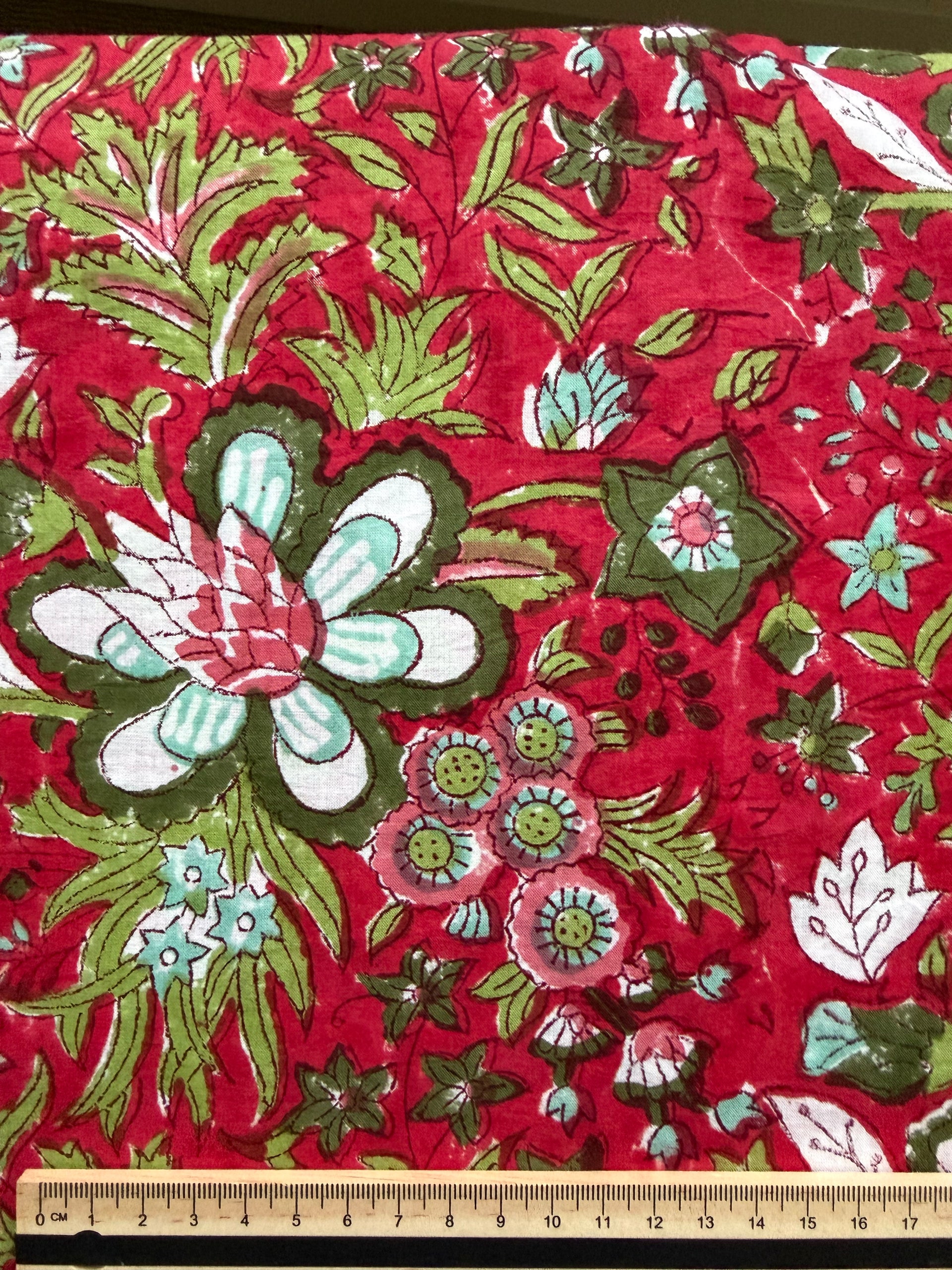 Floral fabric with green and white flowers on a red background, measured by a ruler.