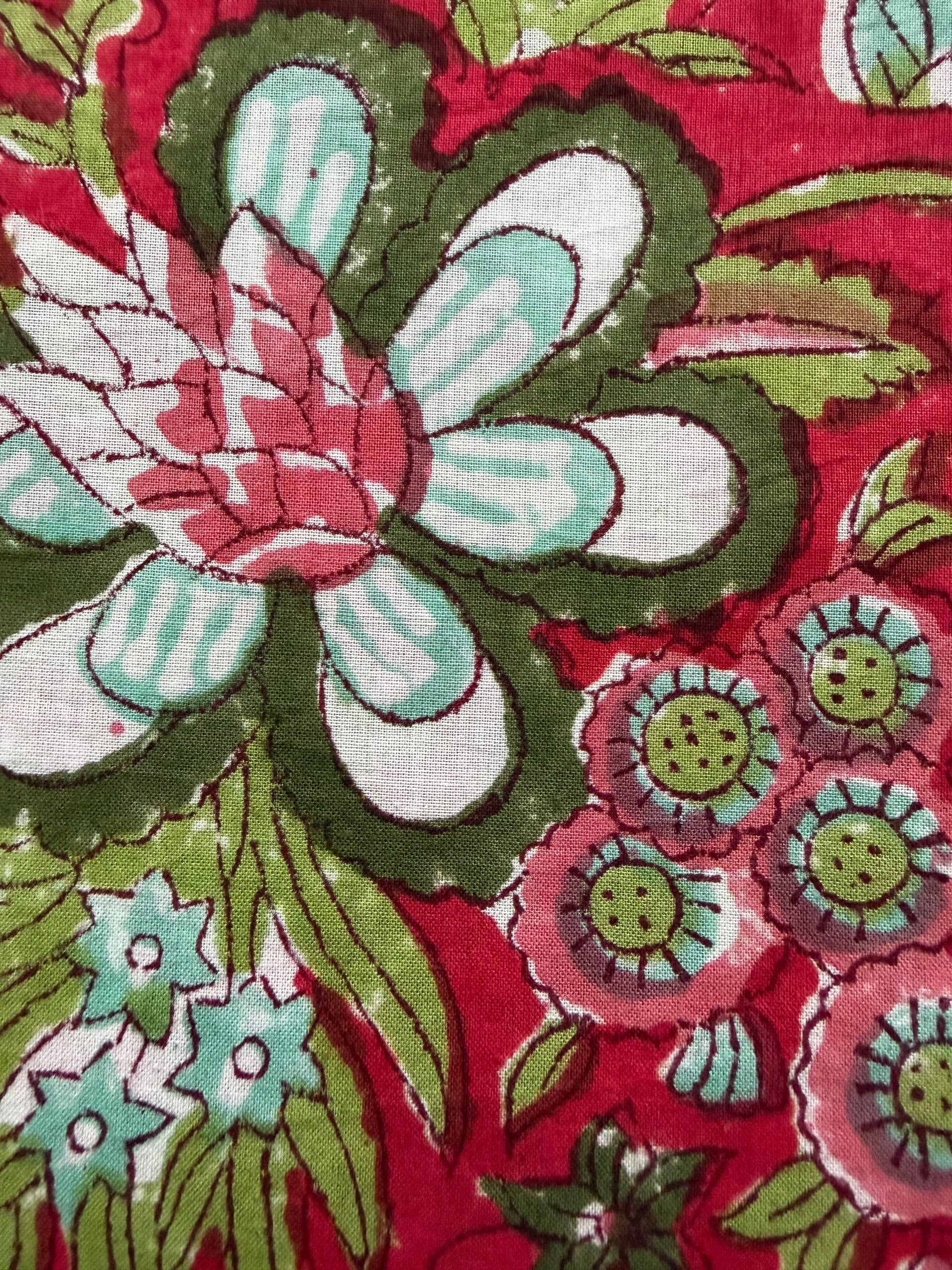 Floral fabric with green and white flowers on a red background, measured by a ruler.