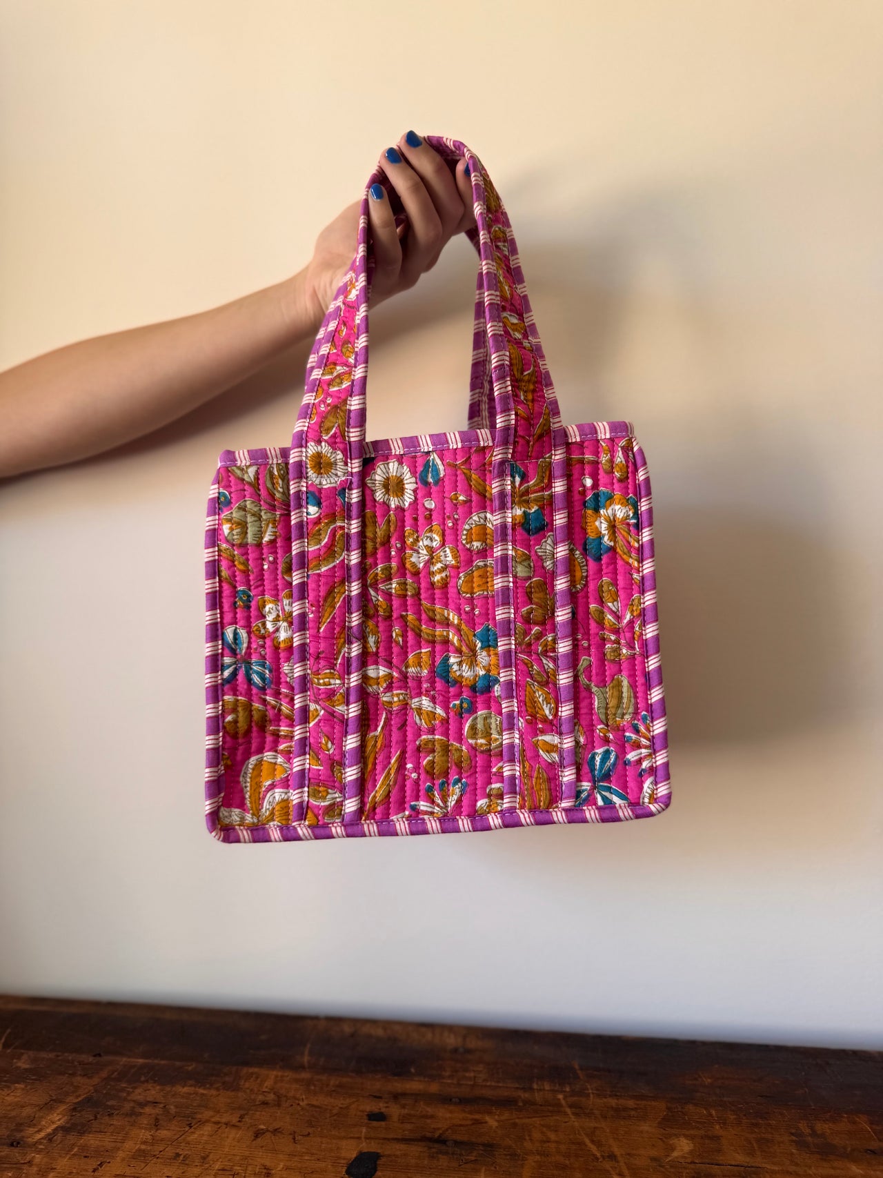 Hand holding a pink patterned bag against a plain background