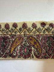 A close-up of a woven textile trim featuring a detailed paisley pattern in dusty pink, olive green, and gold on a cream background.