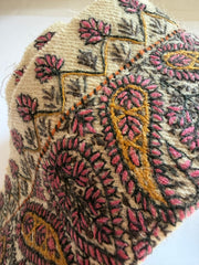 A close-up of a textured fabric featuring a detailed paisley and floral pattern in pink, mustard yellow, and dark brown on a cream-colored base.
