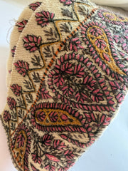 A close-up of a textured fabric or rug featuring a detailed paisley and floral pattern in pink, gold, and dark brown on a cream background.