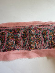 A close-up of a pink woven textile with a multicolor paisley and floral pattern, laid against a plain off-white background.