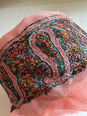 A close-up of a pink sheer mesh fabric with intricate multicolor embroidery, featuring floral and paisley-like patterns in pink, teal, orange, yellow, and black.