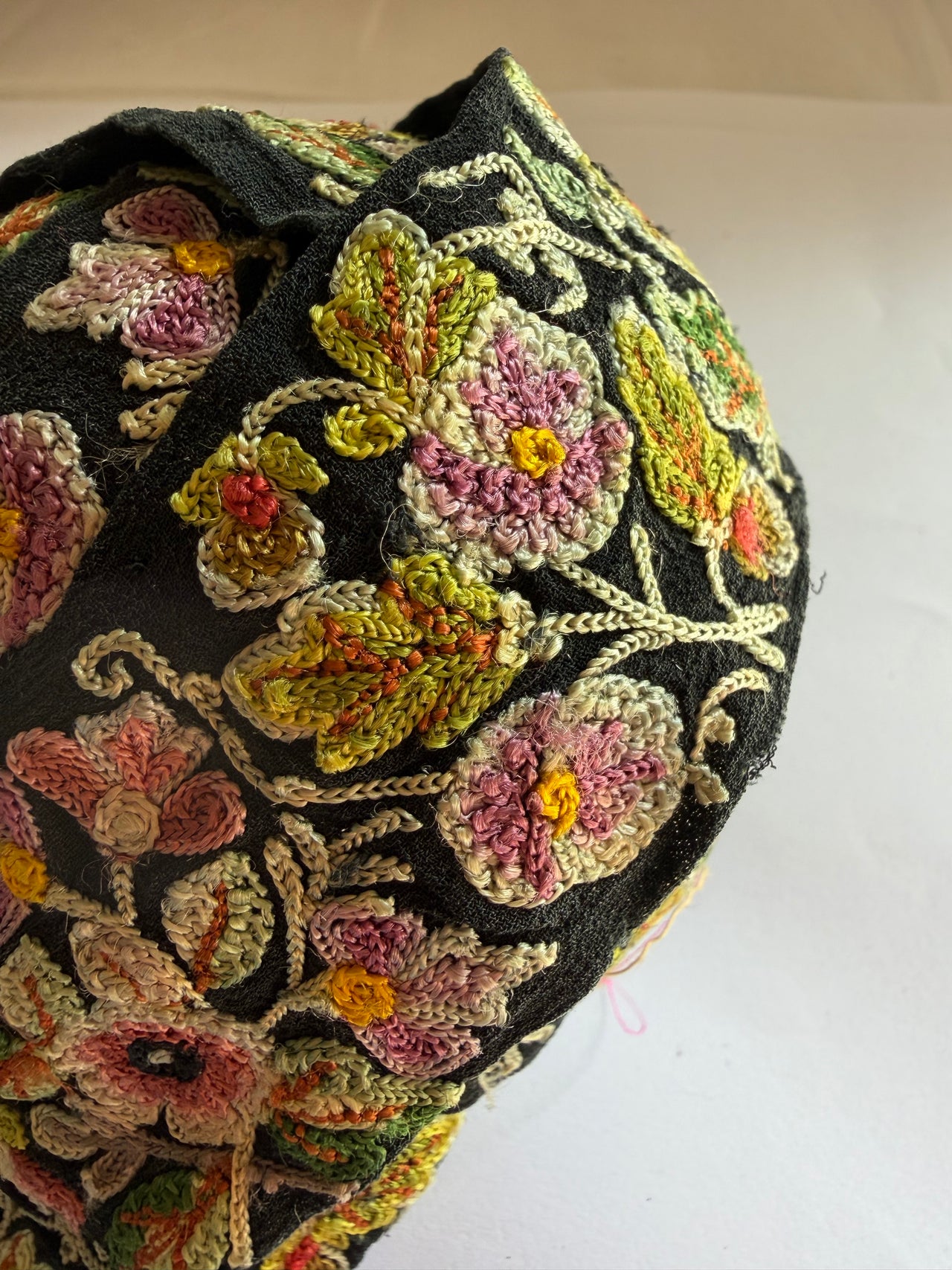 A close-up of a black fabric headscarf featuring intricate, colorful floral embroidery with pink, green, yellow, and orange threads.