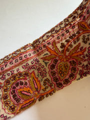 A close-up of a patterned textile or fabric strip with an ornate paisley and floral design in pink, orange, brown, and beige tones on a plain light background.
