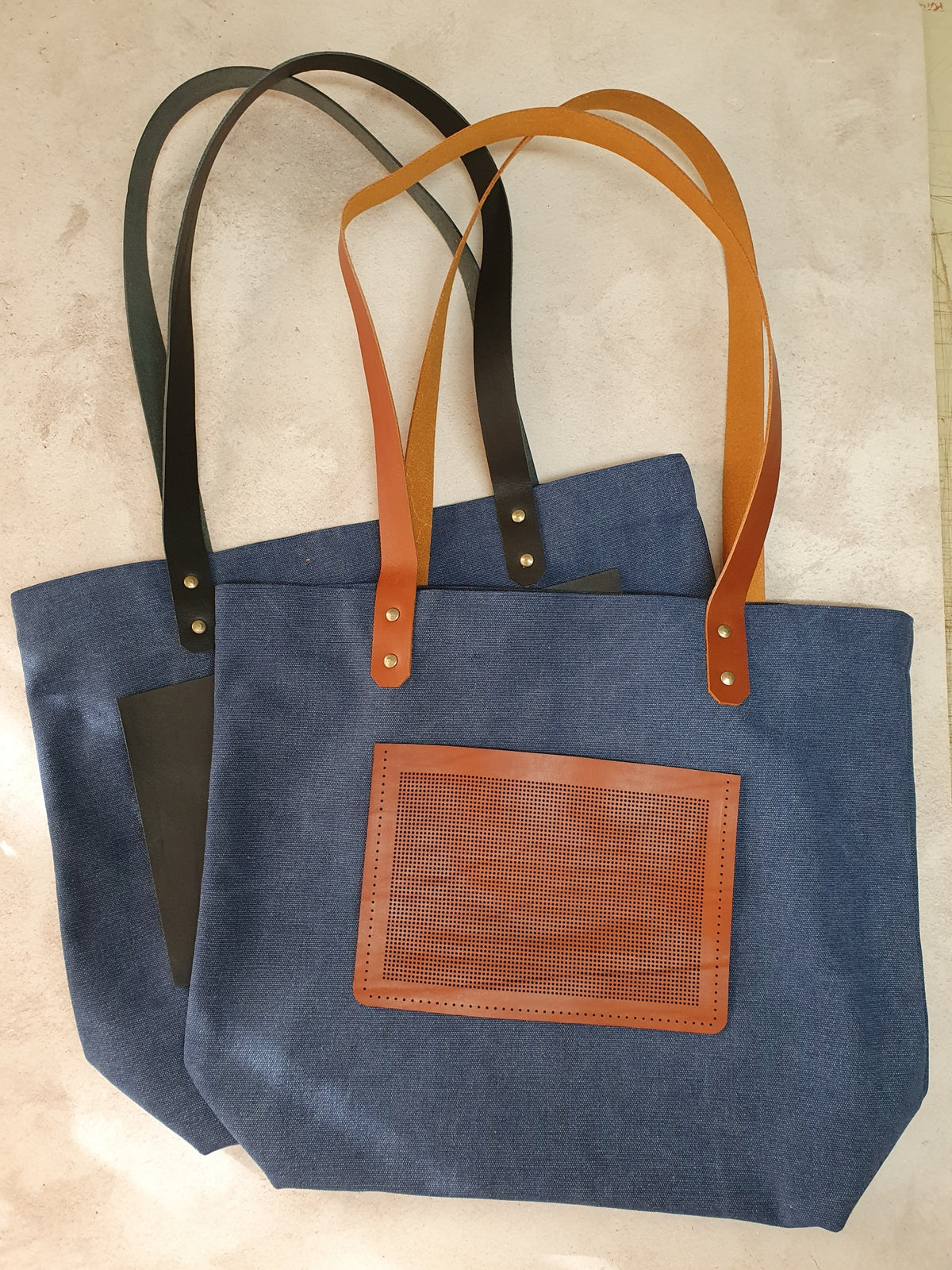 Blue cross-stitch tote bags with leather stitching panels and black or tan handles