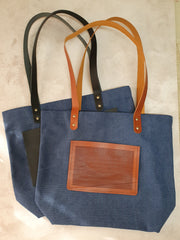 Blue cross-stitch tote bags with leather stitching panels and black or tan handles